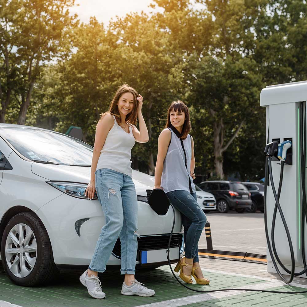 Zwei Frauen lehnen an einem Auto, das an einer Elektro-Ladestation steht