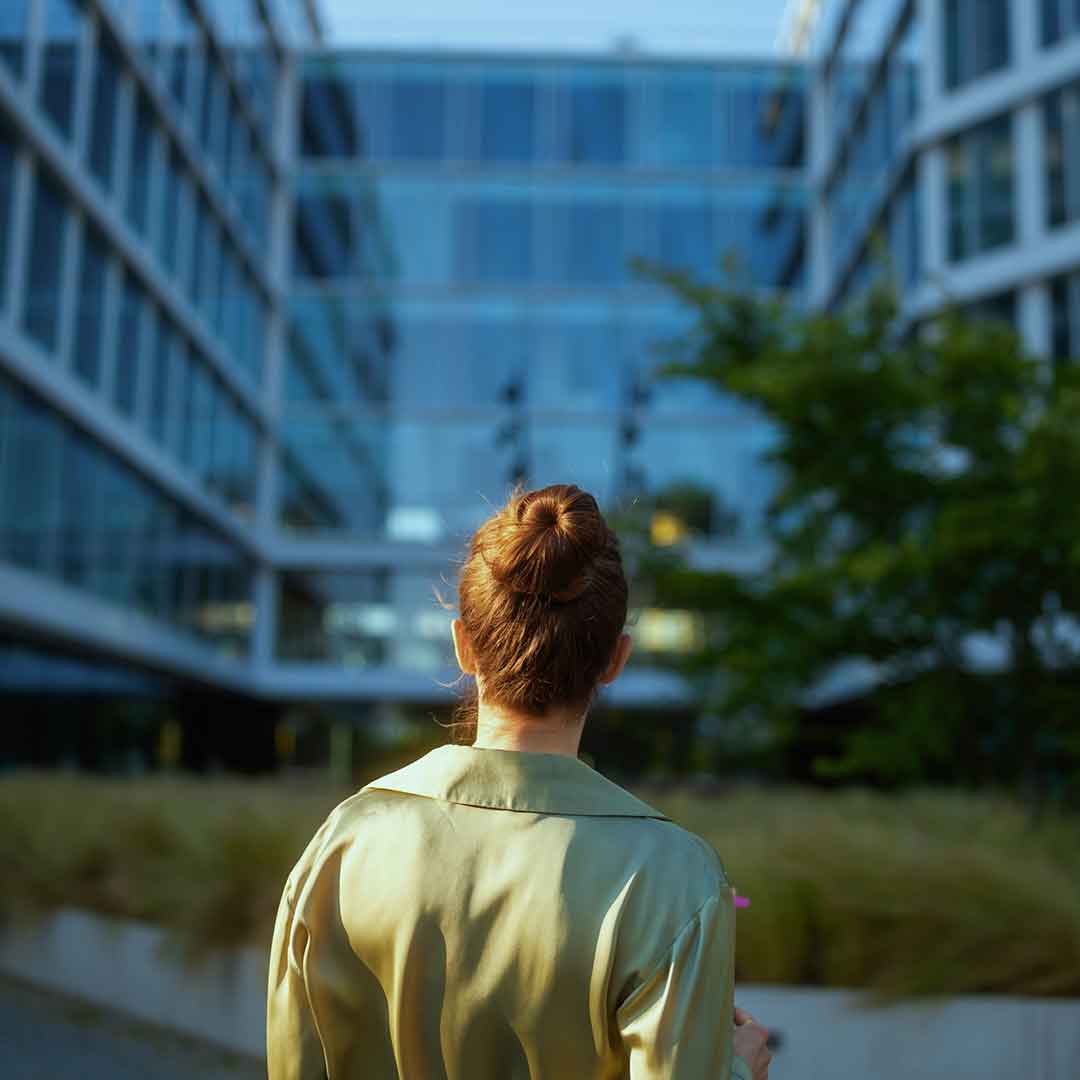 Ein Frau steht mit dem Rücken zur Kamera vor einem großen Büro-Komplex