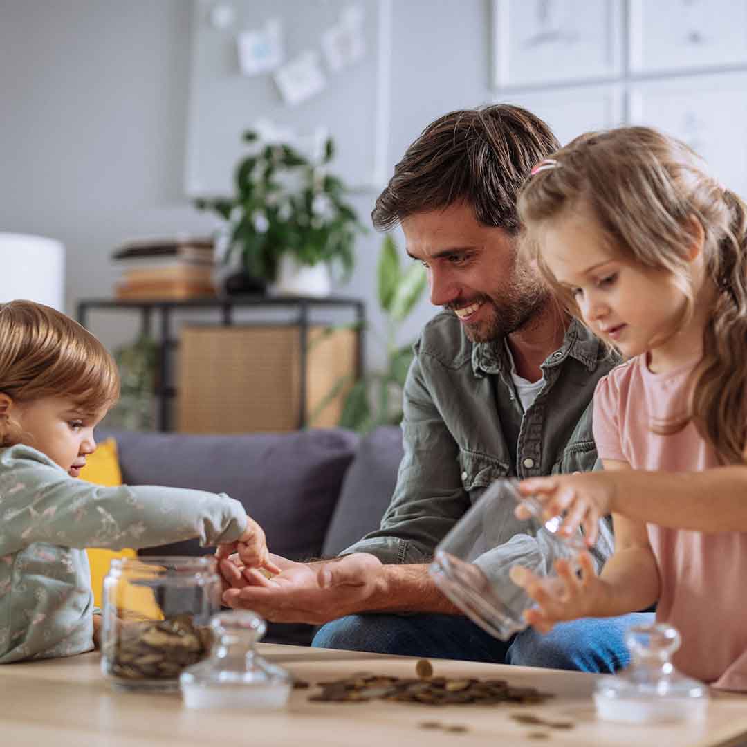 Ein Vater sitzt gemeinsam mit seinen zwei Kindern an einem Tisch mit vielen Münzen