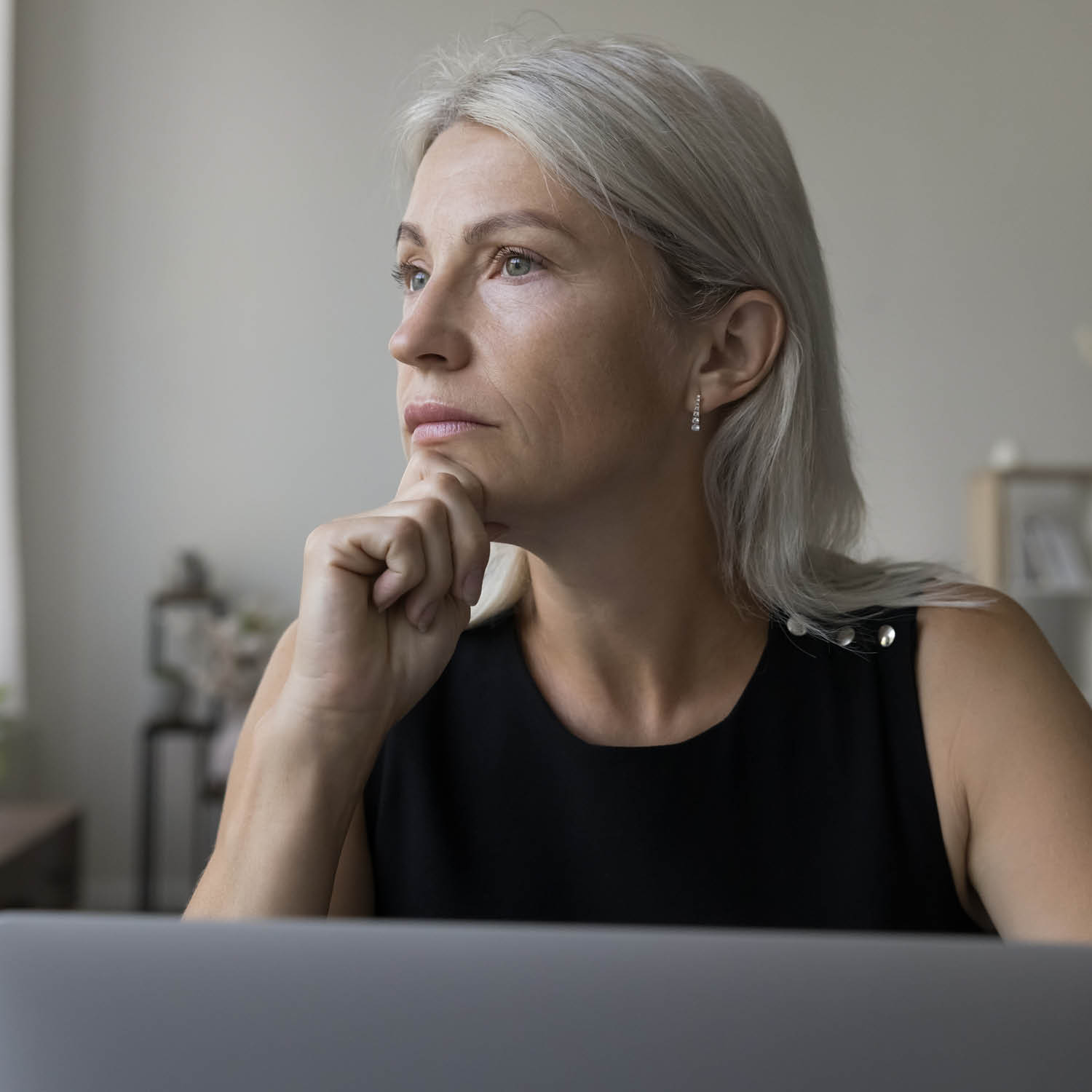 Frau mittleren Alters in nachdenklicher Pose vor einem Laptop