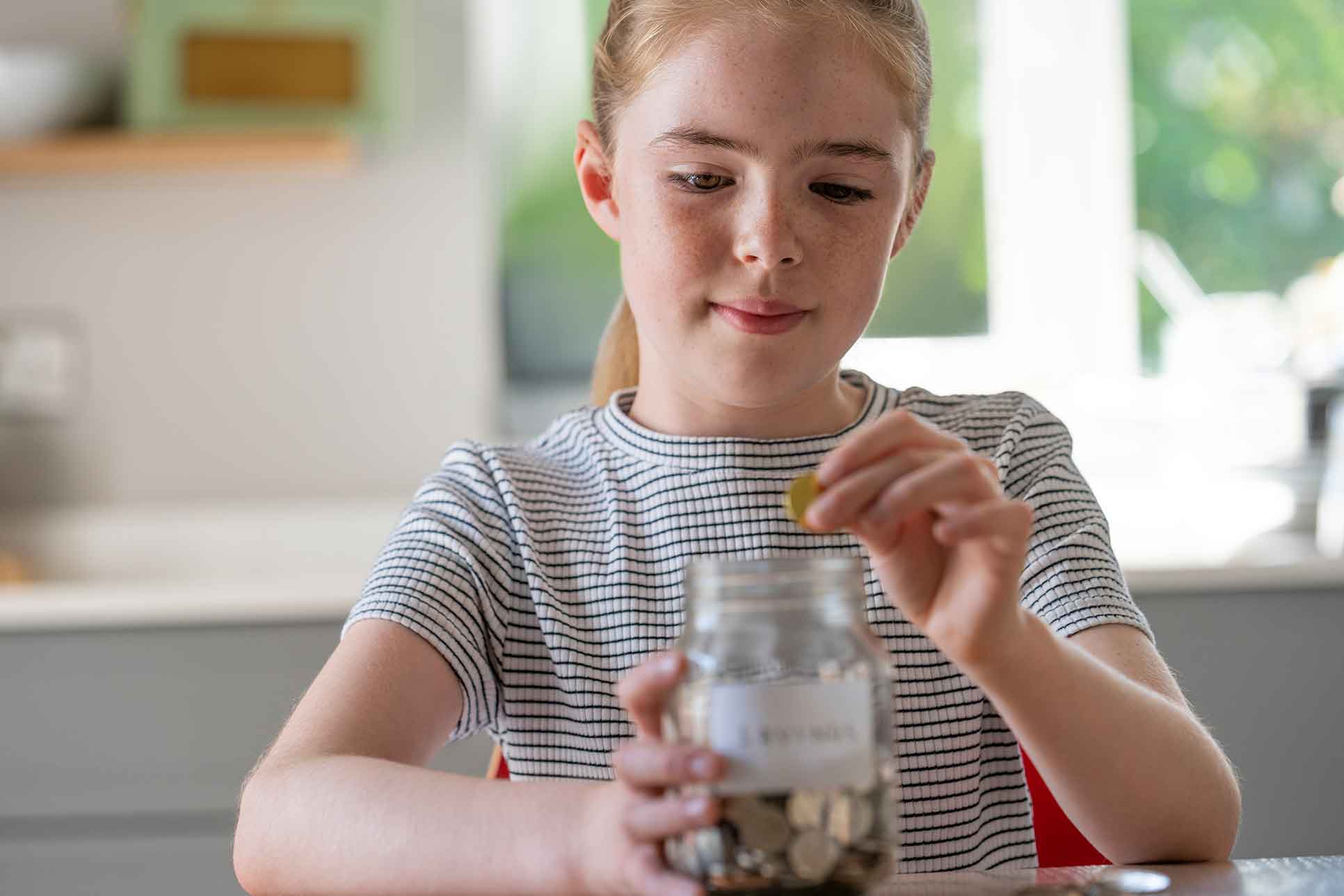 Ein junges Mädchen wirft Geld in eine Glasdose