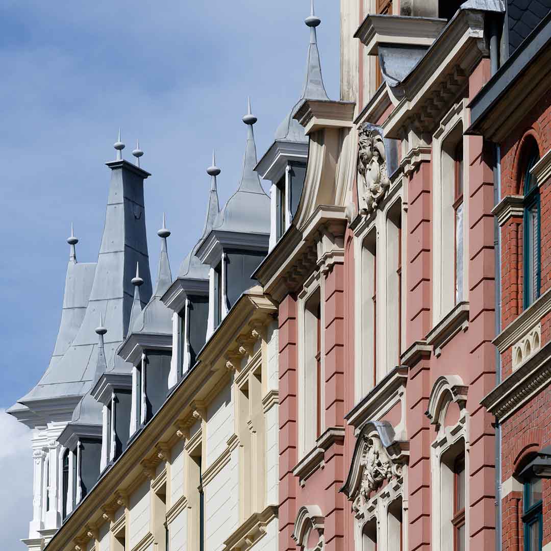 Kunstvolle pastellfarbene historistische Fassaden mit Erkern und Türmchen vor einem blauen Himmel.