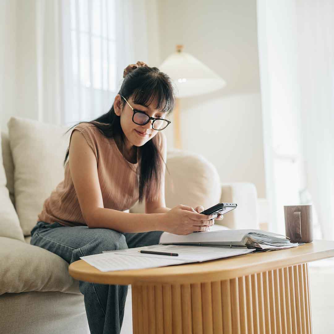 Junge Frau sitzt im Wohnzimmer und plant ihr Budget mit einem Taschenrechner auf ihrem Smartphone