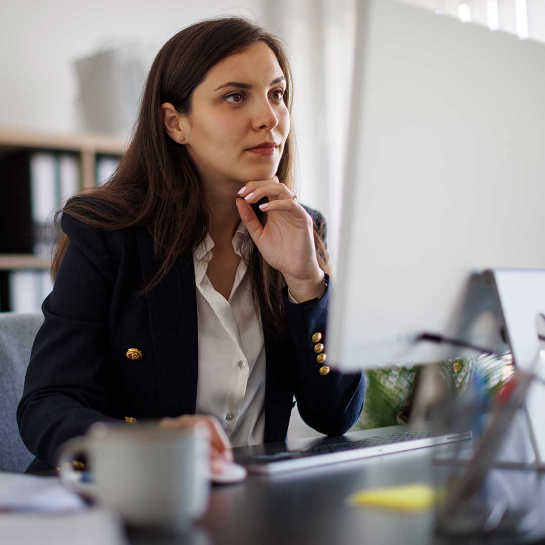 Junge Business Frau sitzt an ihrem Arbeitsplatz und schaut in ihren Laptop