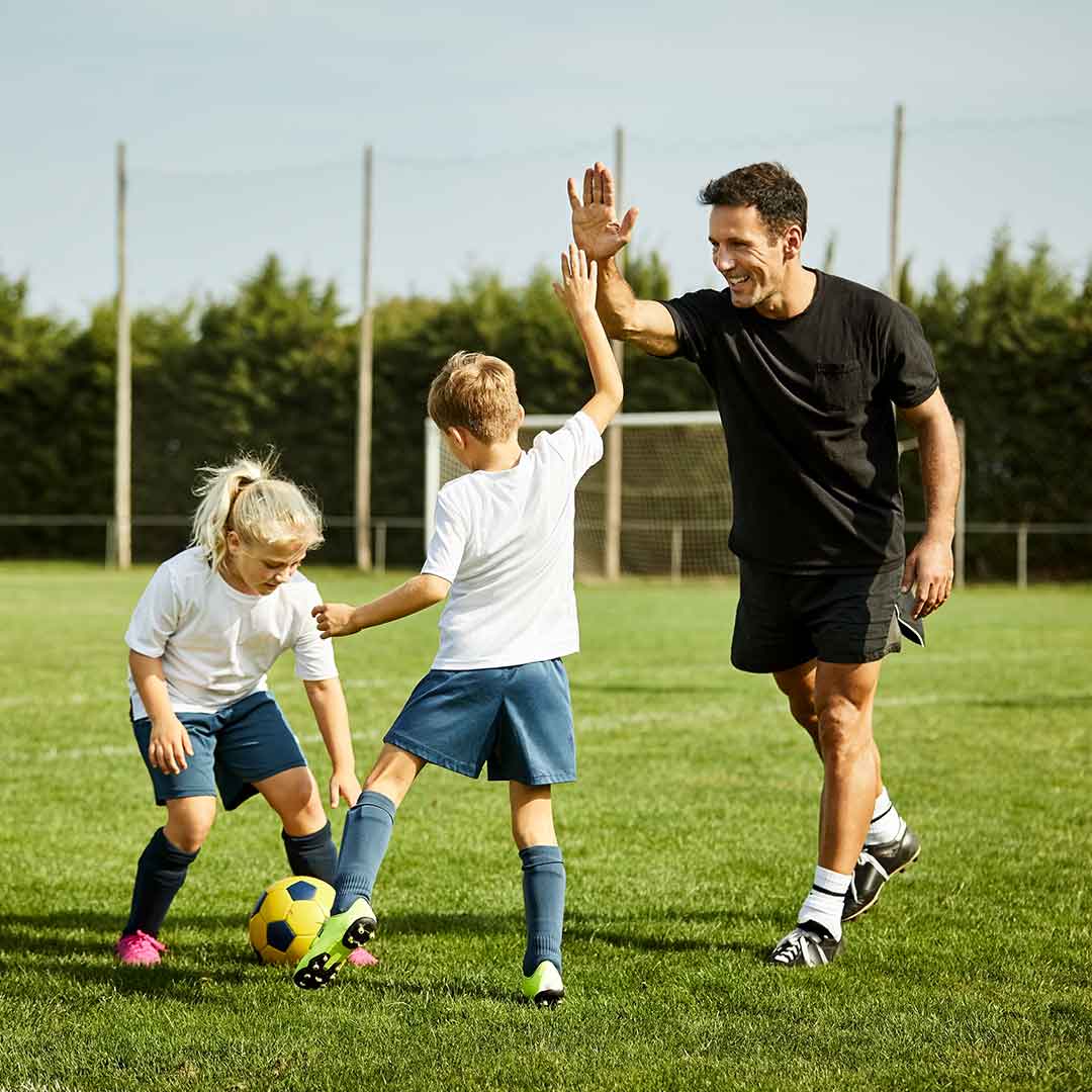 Fussballtrainer klatscht einen jungen Fußballer auf dem Rasen ab