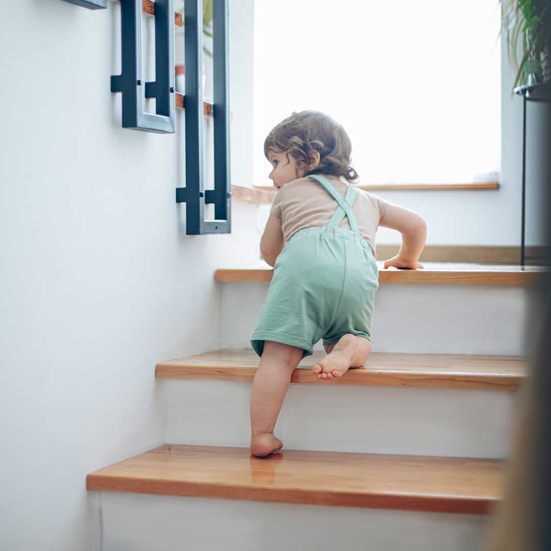 Ein Kleinkind krabbelt in Latzhose eine Treppe hinauf.